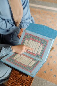 A person pointing at a Quran page, symbolizing Islamic faith and devotion indoors.